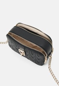 Sac en bandoulière en simili cuir matelassé noir, à deux compartiments zippés, avec quincaillerie en ton doré, une bandoulière en chaîne, texture lisse et doublure de couleur neutre.