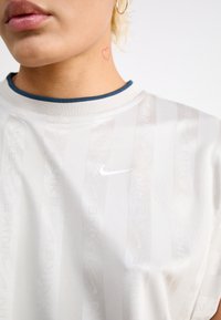 Nike athletic shirt in light beige with textured stripes and logo. Features a contrasting blue collar and a smooth, breathable fabric.