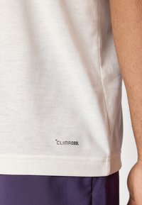 Hvit T-skjorte laget av myk bomullsstoff, med en rund hem og en trykt "CLIMACOOL"-logo nederst til høyre.