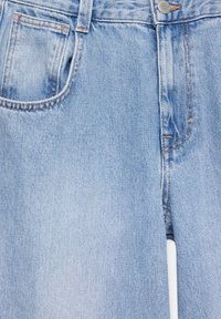 Un jean en denim bleu clair présente un design classique avec une poche frontale, des surpiqûres en cuivre et une fermeture à bouton métallique. La texture est douce.