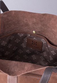 Brown suede interior of a bag with a brown fabric lining featuring a subtle logo pattern. Includes a snap closure and stitched accents.