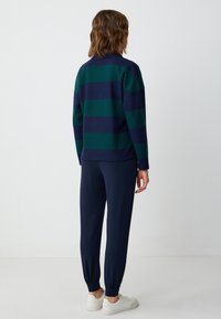Marineblauw en groene gestreepte trui met een relaxed fit, gecombineerd met donker marineblauwe joggers en witte sneakers, gezien vanuit de achterkant.