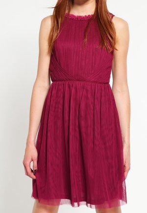 Bordeauxrode mouwloze jurk met geplooid ontwerp, textuurstof en gerimpelde halslijn. Uitlopende rok valt boven de knie.