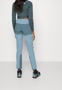 Kvinnors vandringsbyxor i ljusblått med mörkare accenter, i en smal passform och med fukttransporterande tyg. I kombination med svarta träningsskor.