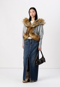 Γκρι κομμένο πουλόβερ με απομίμηση γούνας στον γιακά, συνδυασμένο με μια μακριά τζιν φούστα με μπροστινή σχισμή. Τα αξεσουάρ περιλαμβάνουν μια σκούρα τσάντα και μπεζ μπότες.