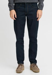 Mørkeblå denimjeans med oransje sømmer, slim fit-design og fem lommer. Brukt med lysebrune suedesko.