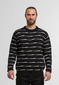 Maglione nero con strisce orizzontali bianche, scollo rotondo, maniche lunghe e polsini e orlo a costine. Realizzato in materiale a maglia testurizzato.