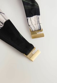 Cinghie in tessuto nero e stampato con clip in metallo dorato alle estremità; presenta cuciture visibili e trame variate.