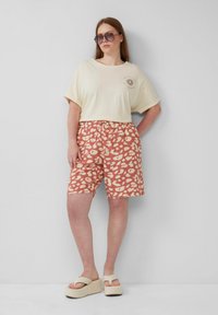 T-shirt crema in cotone con maniche corte e stampa grafica. Pantaloni corti corallo con un motivo a pois. Sandali platform beige chiaro.