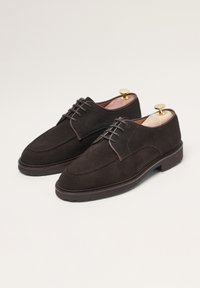 Braune Wildlederschuhe mit glatter Textur, runder Zehenform und Schnürdesign. Mit einer Lederinnensohle und einer Gummisohle ausgestattet. Goldfarbene Schuhspanner sind im Lieferumfang enthalten.