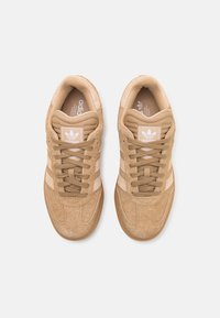 Beige mockasneakers med texturerat tyg, snören och tre vita ränder. Har en vadderad krage och ett mjukt innerfoder.