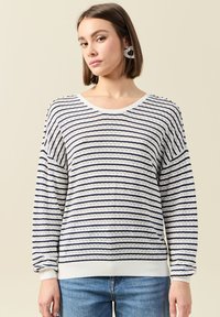 Gestreepte gebreide trui in wit en marineblauw. Heeft een brede ronde halslijn, lange mouwen en geribbelde manchetten. Textuurpatroon met open steken.