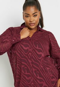 Camicia button-up bordeaux con un motivo trasparente e strutturato che ricorda le onde. Caratterizzata da un colletto e polsini con bottoni, ha una vestibilità morbida.