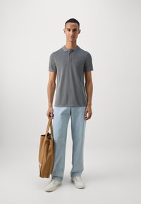 Szary polo z kołnierzykiem, jasnoniebieskie dżinsy, białe sneakersy oraz brązowa torba trzymana w jednej ręce. Prosty design, casualowy wygląd.