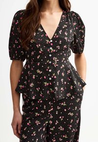 Top peplum negro con mangas cortas abullonadas, escote en V y botones blancos. Presenta un patrón floral con acentos en rosa y azul.