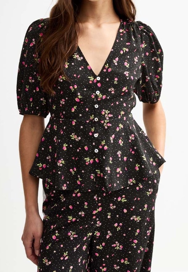 Top peplum negro con mangas cortas abullonadas, escote en V y botones blancos. Presenta un patrón floral con acentos en rosa y azul.