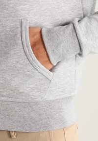 Grå sweatshirt med en mjuk textur, med en framficka, ribbade ärmslut och nederkant. Tyget har ett subtilt melerat mönster.