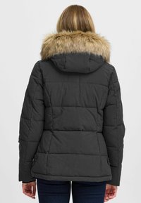 Pildīta melna jakas ar kažokādas oderi kapuci, ar quilted tekstūru, elastīgām piedurknēm un sānu snap aizdares. Rādīta aizmugures skats.