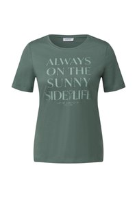 T-shirt en coton vert à manches courtes et col rond, présentant un texte imprimé de tailles variées et des accents métalliques sur le devant.