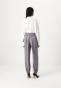 Pull blanc raccourci à manches longues, associé à un pantalon gris avec taille élastique, comportant des poches latérales et des talons noirs.