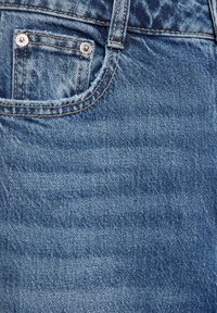 Denim spijkerbroek in een vervaagde blauwtint, met een klein voorvakje, zilverkleurige hardware en zichtbare stikseldetails.