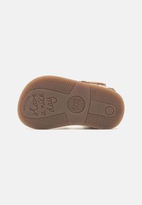 Sole béžové dětské boty s texturou pro lepší grip a nápisy "Mějte hezký den" a "Gios Eppo" na spodní části.