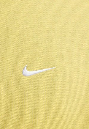Gul atletisk stof med en tekstureret overflade, der har et hvidt broderet Nike Swoosh-logo placeret til venstre.