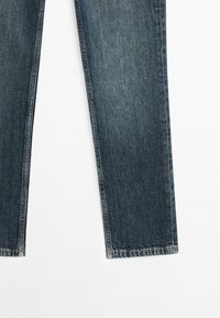 Jambes de jean en denim bleu foncé, coupe droite avec coutures visibles sur fond blanc.