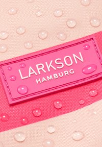 Vattendroppar på rosa tyg med en rosa etikett med texten "Larkson Hamburg" i vita bokstäver.