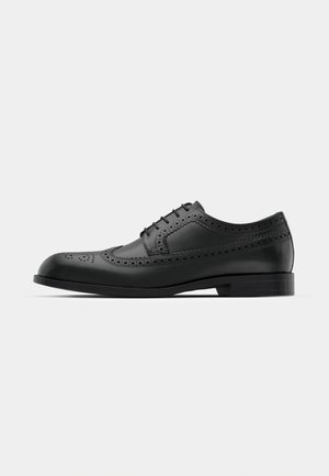 Chaussure élégante en cuir noir avec détails brogués, finition lisse, bout rond et petit talon empilé. Design classique à lacets pour un ajustement sûr.