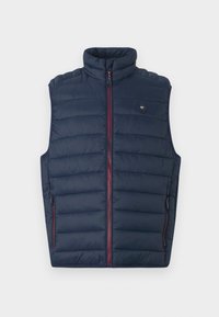 Marineblå puffervest med høy krage, glidelås og røde detaljer. Har horisontalt quiltet mønster og sidelommer. Lett materiale.