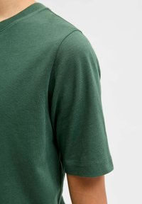 Donkergroen T-shirt met korte mouwen, gemaakt van zachte katoen, met een ronde halslijn en een gladde textuur met minimale stikseldetails.