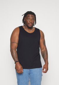 Canotta nera senza maniche in cotone, con scollo rotondo e vestibilità rilassata. Indossata con jeans di denim blu.