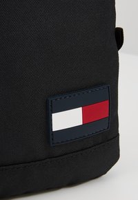 Coin de sac en tissu noir avec un patch logo rectangulaire cousu présentant des blocs de couleurs horizontaux blanc, rouge et bleu marine.