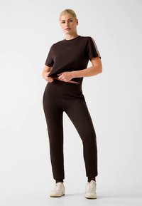 T-shirt en coton noir à coupe décontractée et manches courtes, associée à un pantalon jogger noir avec bandes latérales et taille élastique.