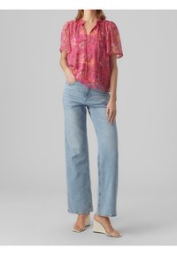 Blouse florale rose en tissu transparent, manches courtes et col en V. Associée à un jean taille haute bleu clair et des sandales compensées beiges.