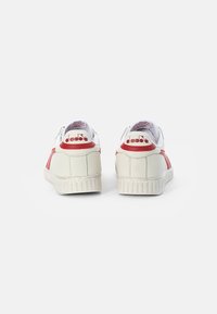 White athletic shoes with red accents, featuring a textured rubber sole, smooth leather upper, and brand logo on the heel.