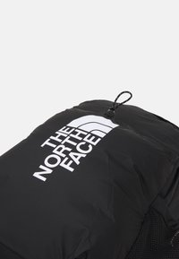 Sac à dos noir avec logo blanc "The North Face" et cordon réglable en haut sur fond blanc uni.