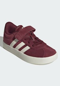 Bordo suède cipele s bijelim prugama, okruglim vrhom i tekstilnom kopčom. Tekstuirani materijal i gumeni potplat za izdržljivost.