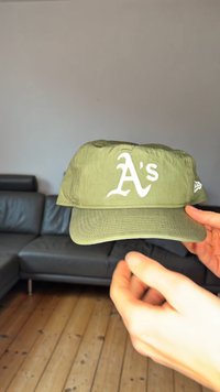 Zelena kapa s zakrivljenim obodom, s bijelim izvezenim logotipom "A's" na prednjoj strani. Lagani materijal glatke teksture.