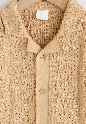 Beige gebreide cardigan met een textuurpatroon, open kraag en twee knopen. Gemaakt van zacht materiaal, met een ademend ontwerp.
