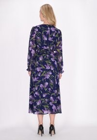 Rochie lungă de culoare bleumarin, cu flori și irisuri purpurii și frunze verzi. Prezintă talie strânsă, mâneci lungi și manșete volan. Este purtată cu tocuri negre.