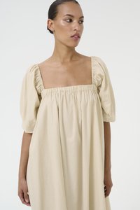Vestido color crema hecho de una tela ligera, con escote cuadrado y mangas abullonadas, recogidas en los hombros para un ajuste relajado.