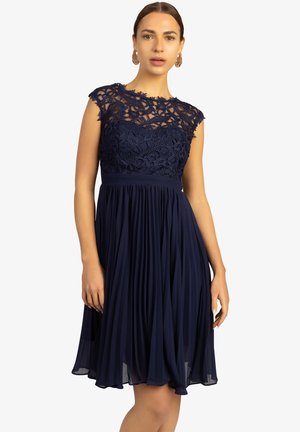 Robe marine avec un délicat corsage en dentelle, des manches chauve-souris et une jupe plissée. Fabriquée en tissu léger avec une texture douce.