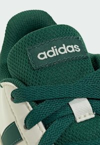 Green mesh upper sneaker featuring a white leather toe cap, matching laces, and an Adidas logo label stitched on the tongue.