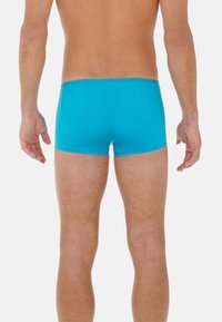 Pantaloni da mare turchesi realizzati in tessuto elasticizzato, con un design aderente e una vita bassa, texture liscia senza motivi o decorazioni visibili.