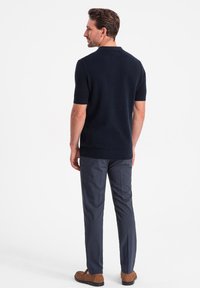 Polo shirt bleu marine à manches courtes en tissu texturé, associé à un pantalon gris foncé ajusté et des chaussures brunes à enfiler.