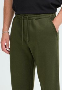 Olivengrüne Sweatpants mit elastischem Bund, verstellbarem Kordelzug, Seitentaschen und weichem, strukturiertem Stoff.