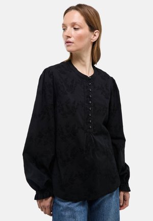Blouse noire à manches longues avec broderie florale, col rond et boutonnage à l'avant. Le tissu est doux avec une finition légèrement texturée.