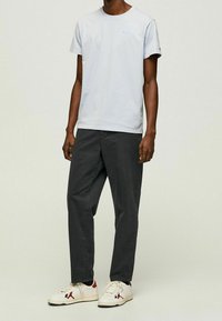 Jasnoniebieska bawełniana koszulka z okrągłym dekoltem, zestawiona z ciemnoszarymi spodniami i białymi trampkami z czerwonymi akcentami w klasycznym stylu.